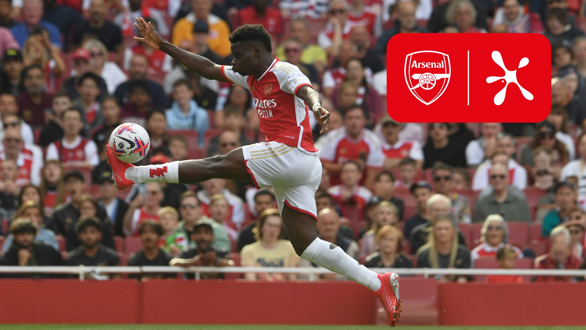 Arsenal forward Bukayo Saka, in an Arsenal kit, kicking a football in front of a crowd.