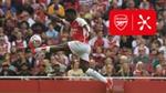Arsenal forward Bukayo Saka, in an Arsenal kit, kicking a football in front of a crowd.