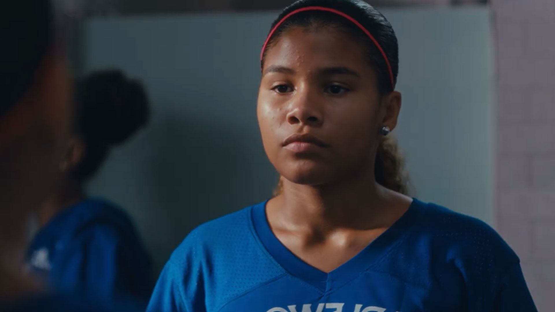 A picture of a girl with a red hair band wearing a blue sports top.