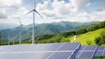 Wind turbines standing tall over a group of solar panels, within a field of grass.