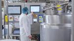 Ice cream factory worker in a white lab coat and hairnet attending a machine that’s part of the manufacturing process