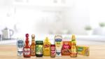 A selection of well known food and condiment brands, including Hellmann’s mayonnaise, Frank’s RedHot, Cholula Hot Sauce, Knorr seasonings, French’s mustard, and condiments, arranged side by side on a wooden table.