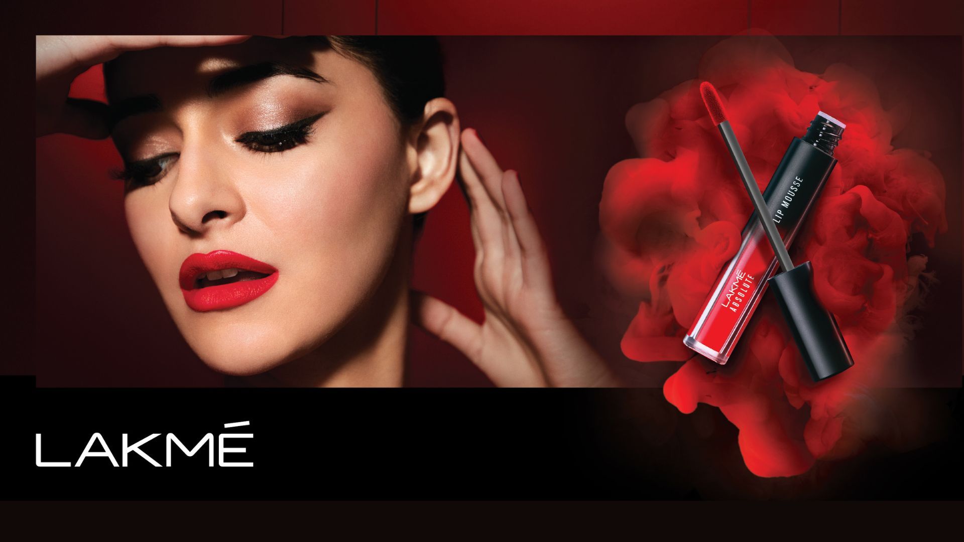 A woman with bold red lips and smokey eye make-up gazes away from the camera, holding a tube of Lakmé lip mousse.