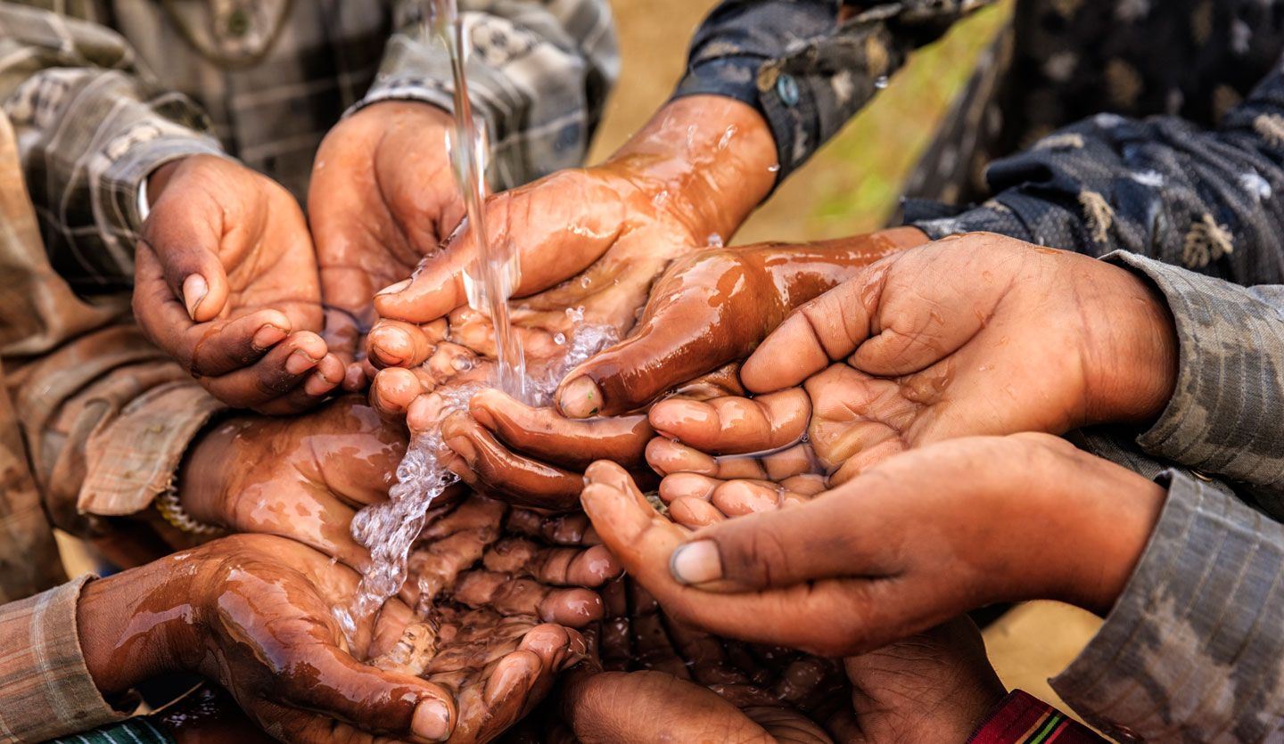 Children bring their hands together to hold some flowing water.