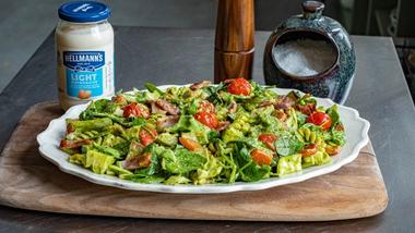 Jar of Hellmann’s Light Mayonnaise next to a plate of salad with a pepper mill and salt pot in the background.
