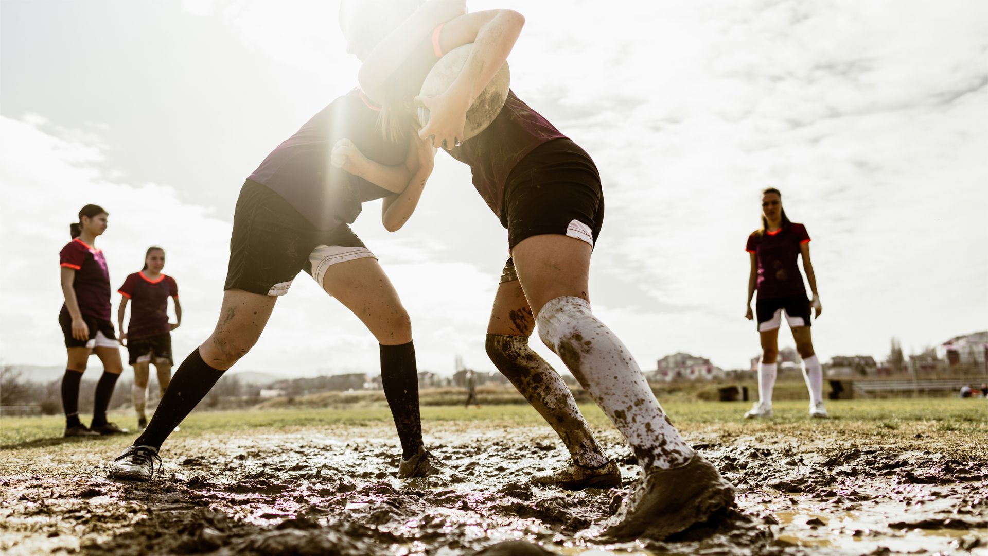 A group of people playing rugby in a very muddy field.