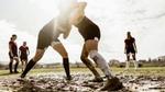 A group of people playing rugby in a very muddy field.