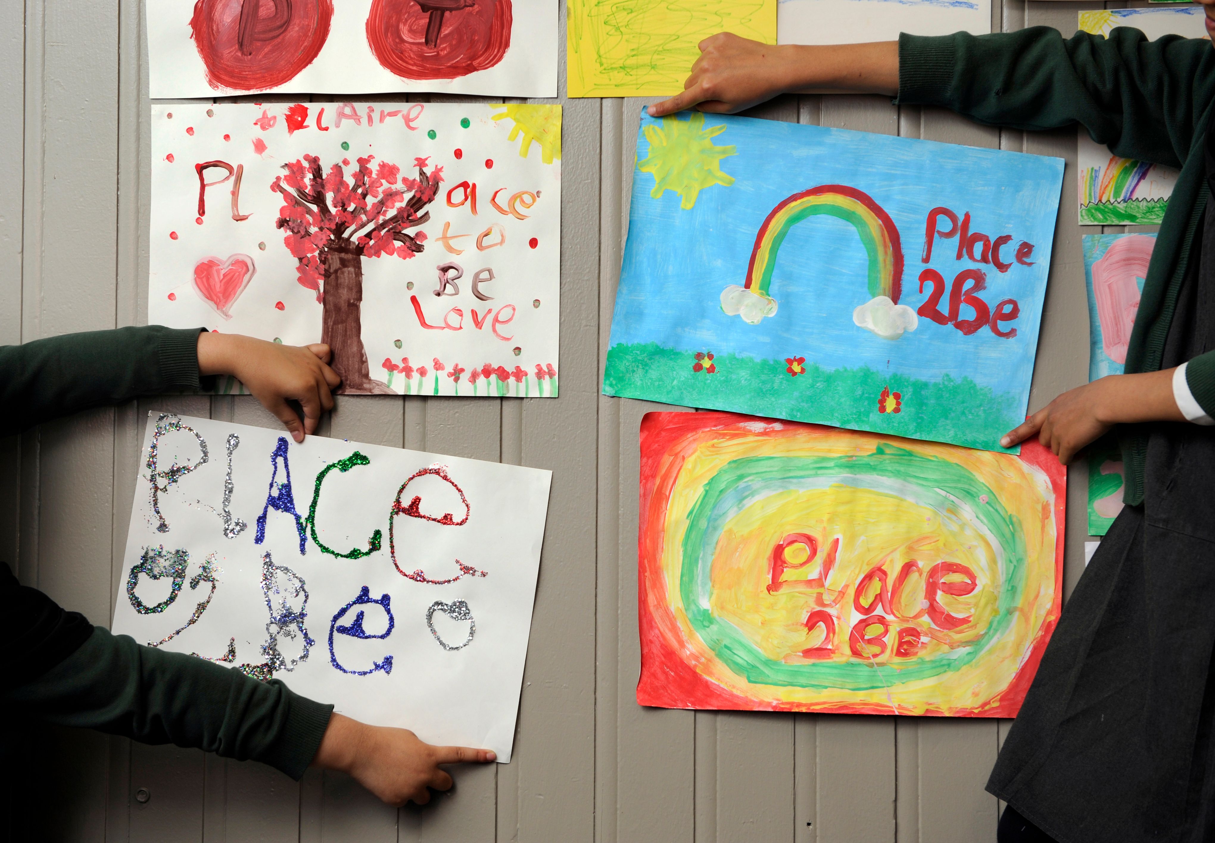 children’s hands pin pictures with place2be written on them onto a wall