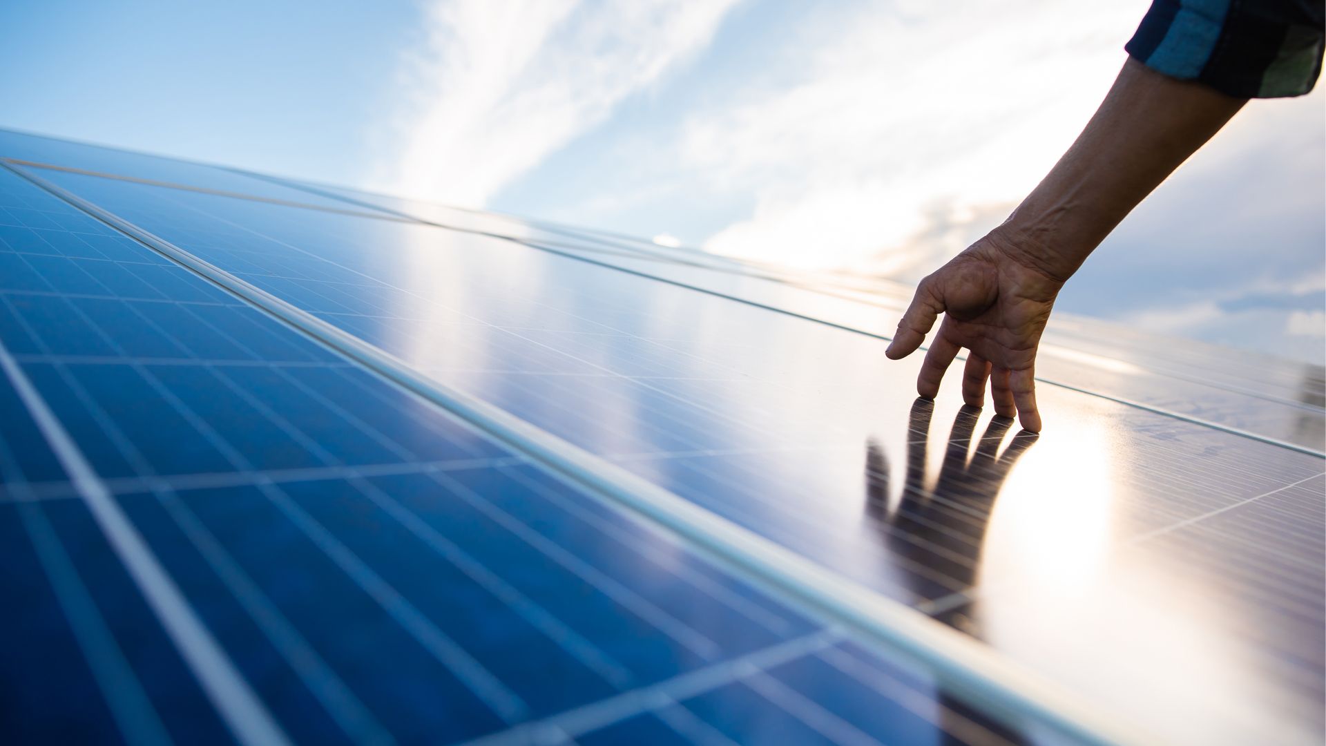 A close up of solar panela with the sun reflecting on it. A hand reaches towards it