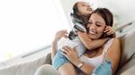 A woman laughing on a couch while a young girl hugs her tightly
