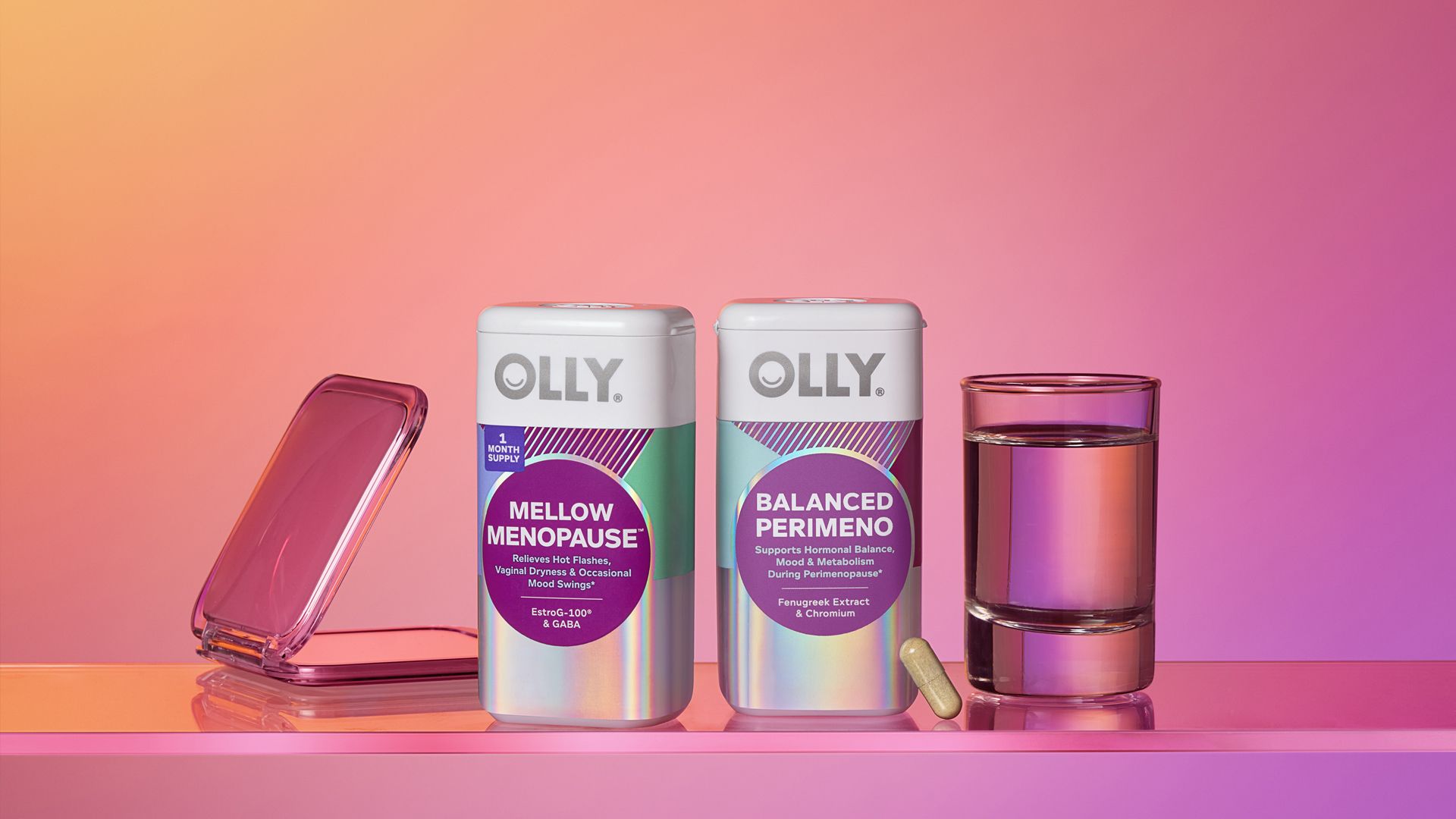 Two bottles of OLLY supplements – Mellow Menopause and Balanced Perimeno – on a reflective surface against a pink gradient background. A single capsule sits in front of the Balanced Perimeno bottle, with a closed pink compact mirror on the left and a glass of water on the right.