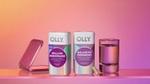 Two bottles of OLLY supplements – Mellow Menopause and Balanced Perimeno – on a reflective surface against a pink gradient background. A single capsule sits in front of the Balanced Perimeno bottle, with a closed pink compact mirror on the left and a glass of water on the right.