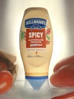 Bottle of Hellmann’s Spicy Mayonnaise Dressing with chili pepper graphics, placed upright on a surface with fresh tomatoes around it.