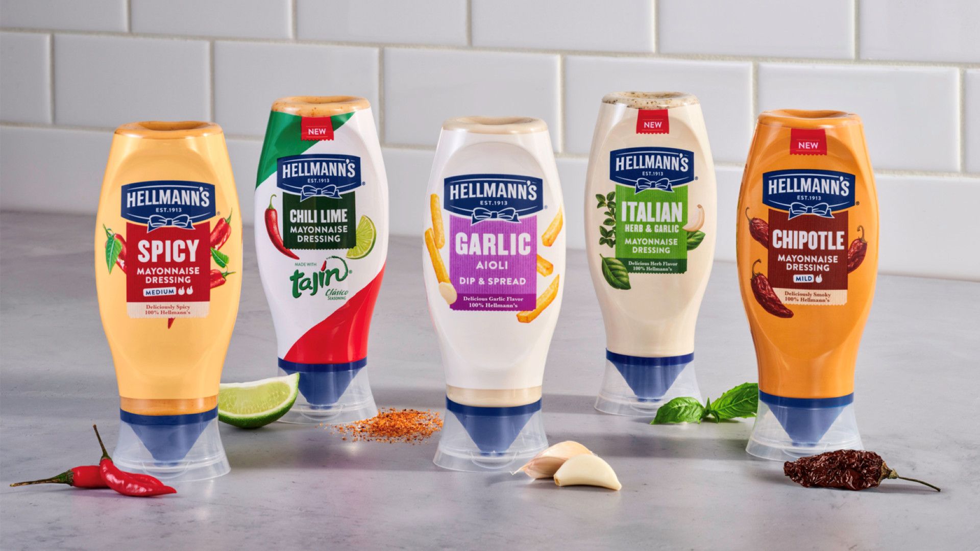 A display of Hellmann’s flavoured mayonnaise on a counter top. Flavours from left to right include: Spicy, Chilli Lime, Garlic Aioli, Italian Herb & Garlic, Chipotle.