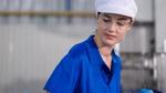 A worker wearing a blue uniform, a white cap, and clear safety glasses in an industrial setting.